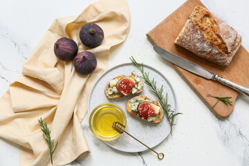 Plate of delicious fig bruschetta with blue cheese and bowl of honey on white background