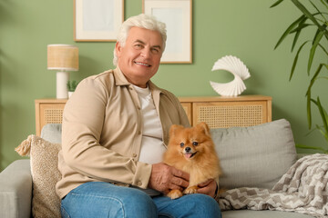 Happy senior man with cute Pomeranian dog sitting on sofa at home