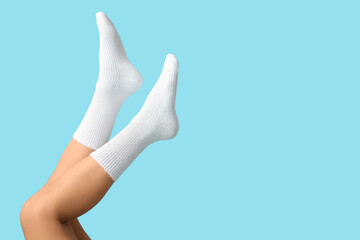 Legs of young woman in white cotton socks on blue background