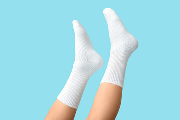 Legs of young woman in white cotton socks on blue background