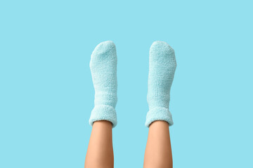 Legs of young woman in warm blue socks on color background