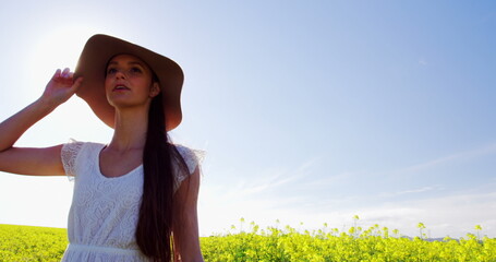 Happy woman wearing hat and walking in mustard field on a sunny day