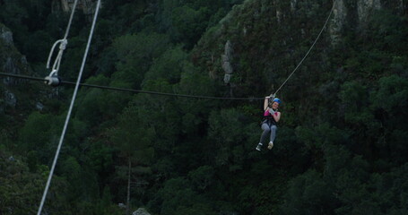 Rear view of a young Caucasian woman zip lining on a sunny day in mountains, slow motion