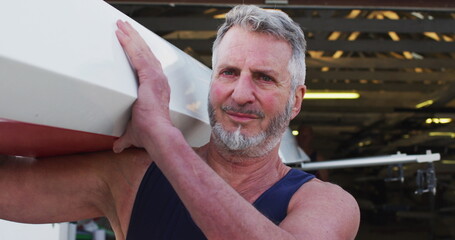 Portrait of senior caucasian man carrying a rowing boat
