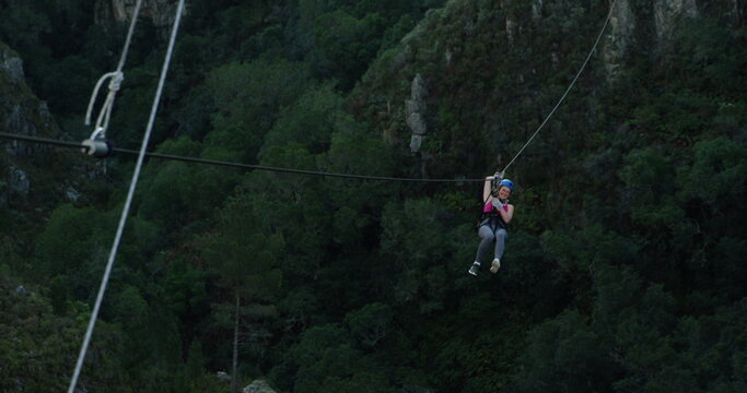 Rear view of a young Caucasian woman zip lining on a sunny day in mountains, slow motion - Powered by Adobe