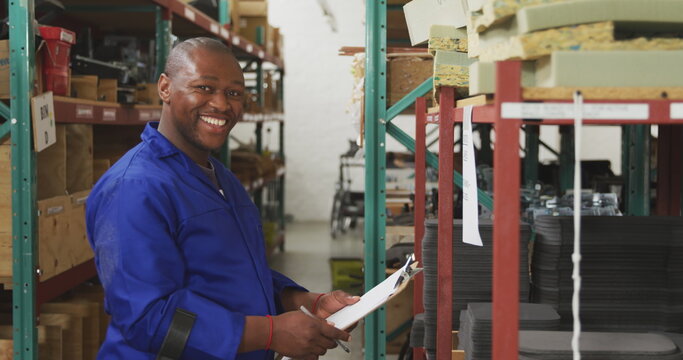 Side view of an African American male worker in a storage warehouse at a factory making wheelchairs,