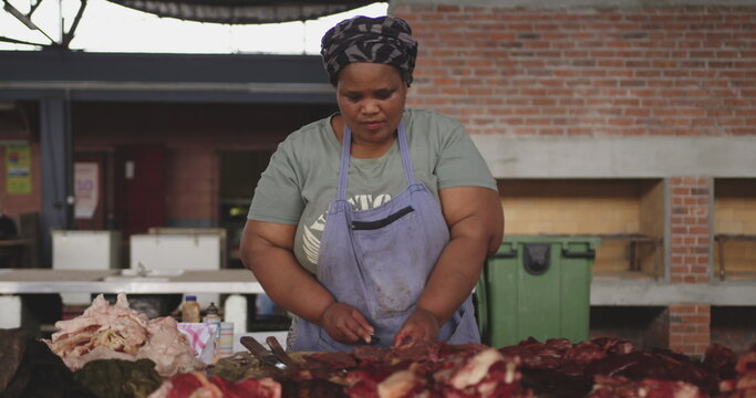 Front view of an African female butcher wearing a headscarf in a township workshop, cutting fresh me - Powered by Adobe