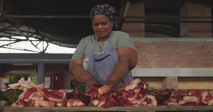 Front view of an African female butcher wearing a headscarf in a township workshop, selecting and pi
