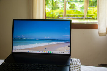 a laptop displaying a beach wallpaper, complemented by sunlight streaming through the window with lush greenery outside