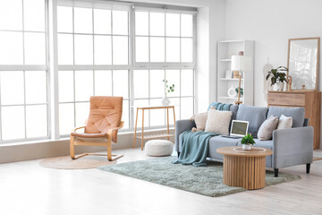 Interior of light living room with laptop on sofa and armchair