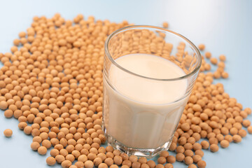 水色の背景に大豆と豆乳が注がれたガラスコップ