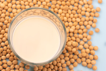 水色の背景に大豆と豆乳が注がれたガラスコップの俯瞰