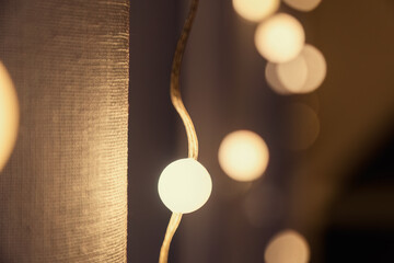 Close-up warm-toned bokeh lights strung along a wire, softly illuminating a textured fabric. Abstract cozy festive backdrop