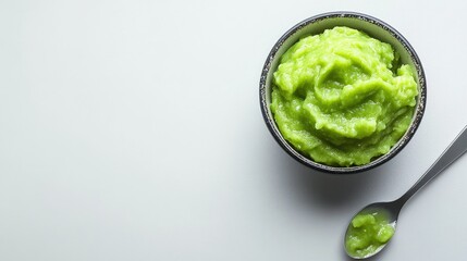 Obraz premium A bowl of vibrant green mash, likely made from peas or avocado, accompanied by a spoon.