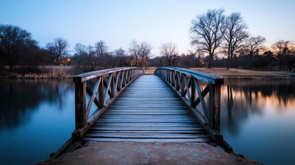 Obraz premium A serene wooden bridge extends over calm waters, surrounded by trees, creating a peaceful landscape at dusk.