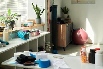 Modern home gym setup with various fitness equipment on shelves and in corners, highlighted by incoming sunlight. Yoga mats, dumbbells, and fitness balls neatly arranged on storage units