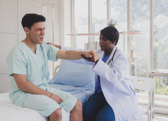 Fototapeta premium Patient caucasian man with woman nurse carer physical therapist black people two person sitting talk helping support give advice and holding hand arm inside clinic hospital indoor room service.