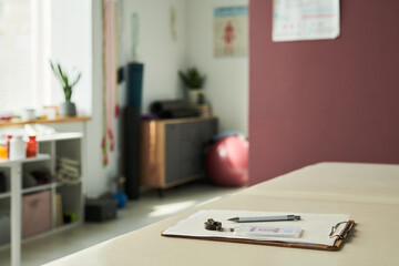 Table in a serene spa room featuring clipboard and pen with sunlight filtering through window alongside plants and equipment creating a calm atmosphere