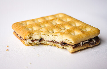 Bitten sandwich biscuit with chocolate filling on white background