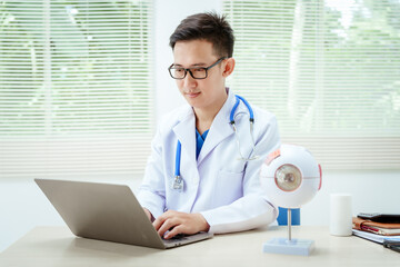 A male doctor wearing glasses sits at a desk in a hospital, explaining eye diseases like glaucoma,...
