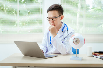 A male doctor wearing glasses sits at a desk in a hospital, explaining eye diseases like glaucoma,...