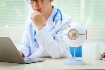 A male doctor wearing glasses sits at a desk in a hospital, explaining eye diseases like glaucoma,...