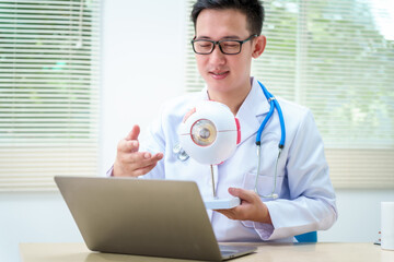 A male doctor wearing glasses sits at a desk in a hospital, explaining eye diseases like glaucoma,...