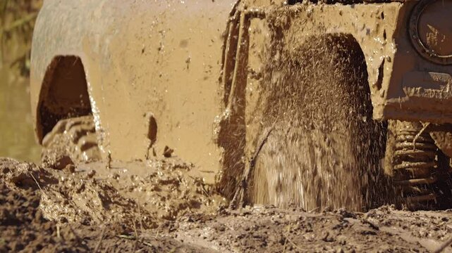 Close-up of the tyres of a muddy SUV stuck in the mud. The wheels spin helplessly, scattering jets of water and clay. Extreme racing. Slow motion