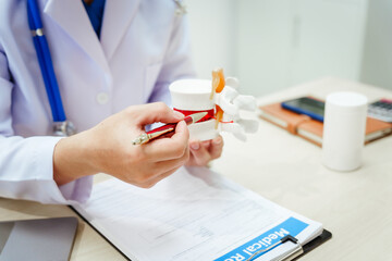 A male doctor wearing glasses sits at a desk, explaining a spine model, discussing spinal anatomy,...
