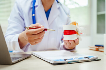 A male doctor wearing glasses sits at a desk, explaining a spine model, discussing spinal anatomy,...