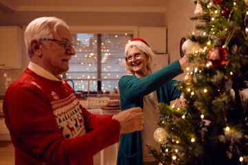 Happy senior couple decorating Christmas tree at home.