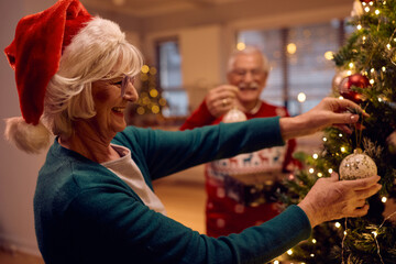 Happy senior woman decorating Christmas tree with ornaments.
