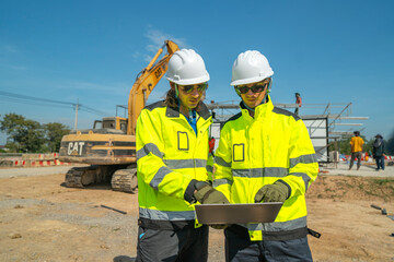An engineer in visibility jacket and helmet standing confidently at a construction site with...