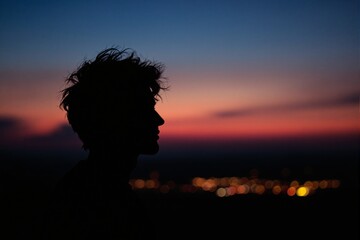 Silhouette of a Young Man Against a Vibrant Sunset Sky with Blurred City Lights