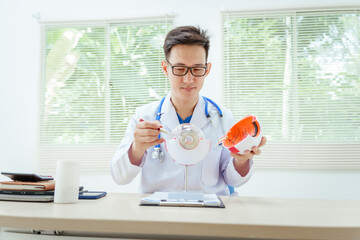 A male doctor wearing glasses sits at a desk in a hospital, explaining eye diseases like glaucoma,...