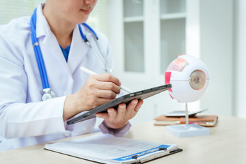 A male doctor wearing glasses sits at a desk in a hospital, explaining eye diseases like glaucoma,...