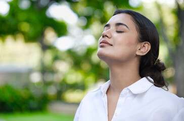 Relaxed happy refreshing young south asian woman taking a deep breath of clean unpolluted air in urban park, good summer, summer wellness, sunlight exposure concept image