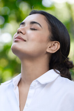 Relaxed happy refreshing young south asian woman taking a deep breath of clean unpolluted air in urban park, good summer, summer wellness, sunlight exposure concept image