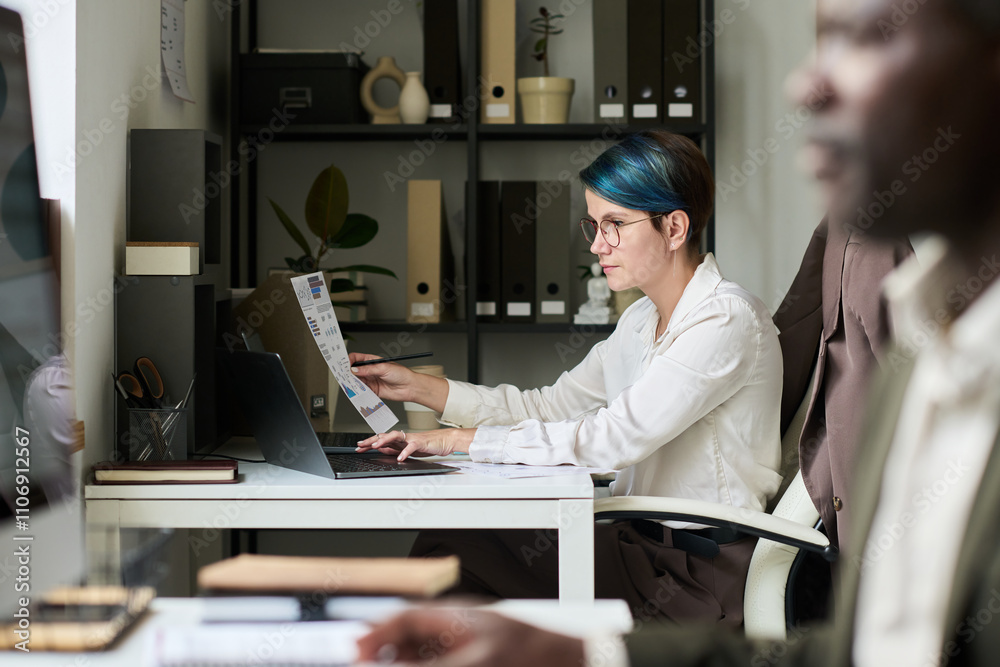 Poster young female trader with financial paper typing on laptop keypad while analyzing economical data by 