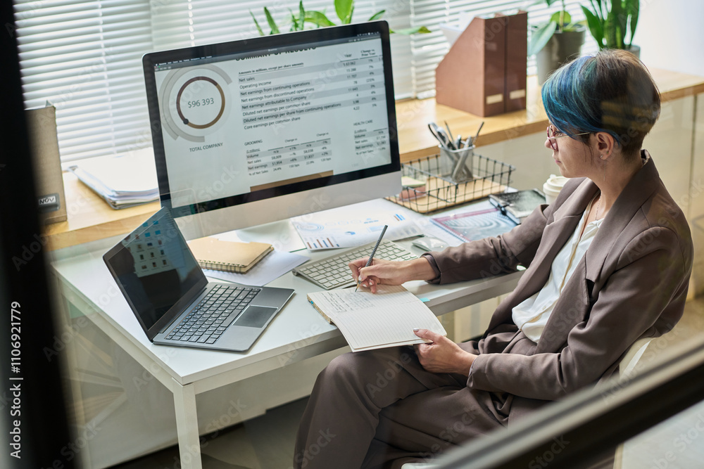 Aufkleber Female broker sitting in front of computer with graphic data on screen, analyzing information and diagram and taking notes
