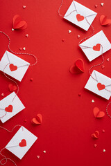 White vertical envelopes with red heart stickers and strings on a red background convey love and romance, perfect for Valentine's Day themes