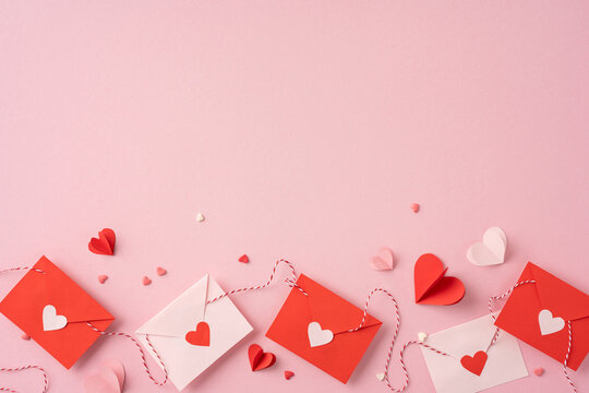 Red and white envelopes with heart decorations on a pastel pink background evoke a romantic valentines day theme
