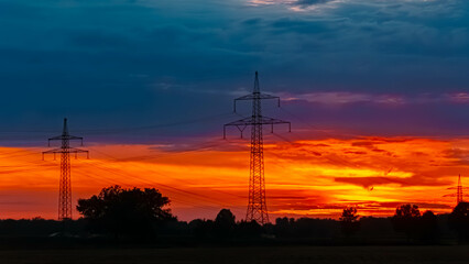 Summer sunset with a dramatic sky and overland high voltage lines near Tabertshausen, Deggendorf, Bavaria, Germany