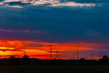 Summer sunset with a dramatic sky and overland high voltage lines near Tabertshausen, Deggendorf, Bavaria, Germany