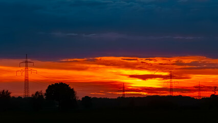 Summer sunset with a dramatic sky and overland high voltage lines near Tabertshausen, Deggendorf, Bavaria, Germany