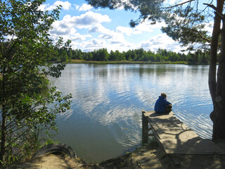 man is resting on the shore of a forest lake