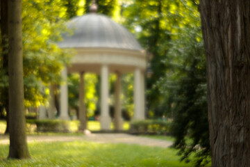 blurred abstraction nature park spring warm light environment space unfocused concept of trees green foliage grass lawn and white marble gazebo landscaped designed classic building object