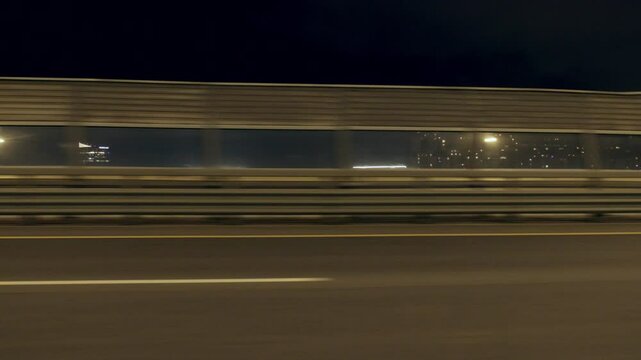 Driving car on high speed in night in city, view from side window, slow motion. Developed road infrastructure in megapolis, urbanistic landscape with modern road fencing, traveling by automobile