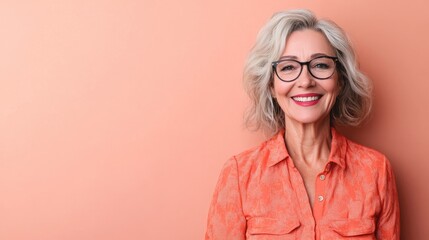 Cheerful beautiful mature woman with a vibrant smile standing against a peach background