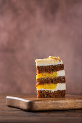 Piece of vegan pumpkin spice or carrot layered cake with coconut cream, walnut and orange confit on a wooden board . Sugar, gluten and lactose free. Vertical orientation.